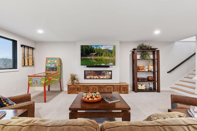 living area with light colored carpet, stairs, a glass covered fireplace, and recessed lighting