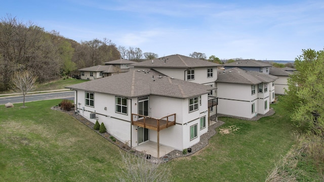 back of house with a lawn, a deck, a residential view, and a shingled roof