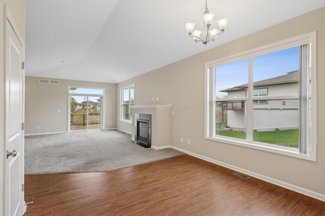 unfurnished living room with lofted ceiling, visible vents, a chandelier, baseboards, and a glass covered fireplace