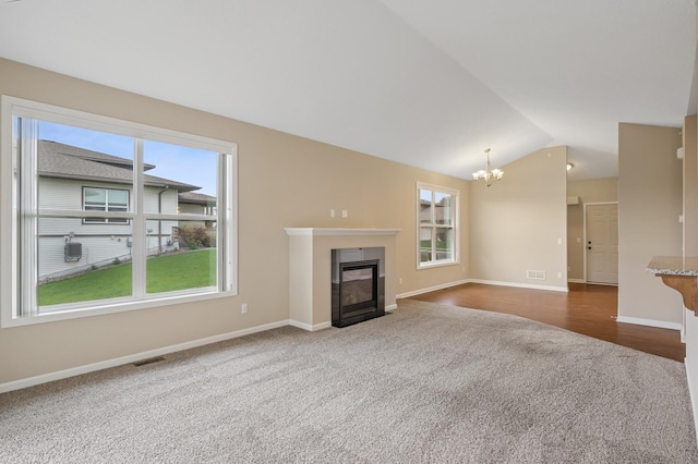 unfurnished living room featuring an inviting chandelier, a wealth of natural light, dark colored carpet, and lofted ceiling