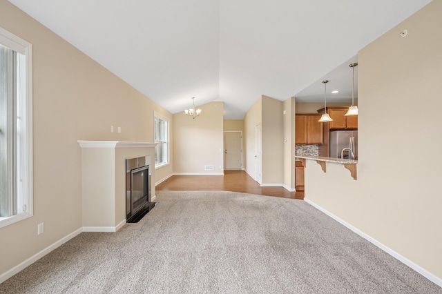 unfurnished living room featuring vaulted ceiling, dark colored carpet, baseboards, and a chandelier