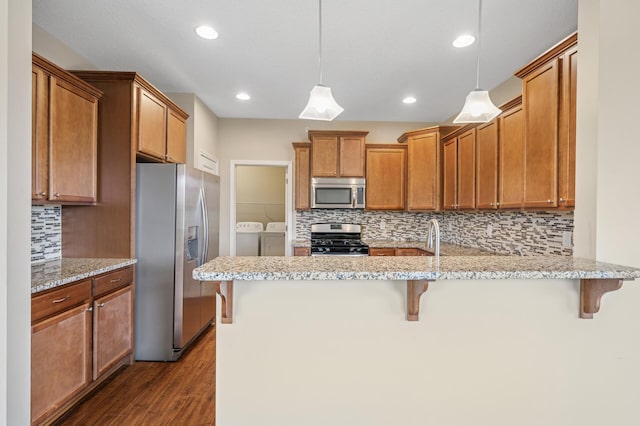 kitchen featuring a peninsula, stainless steel appliances, dark wood-style flooring, decorative backsplash, and washing machine and dryer