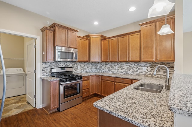 kitchen with a sink, stainless steel appliances, light stone countertops, washer / dryer, and dark wood-style floors