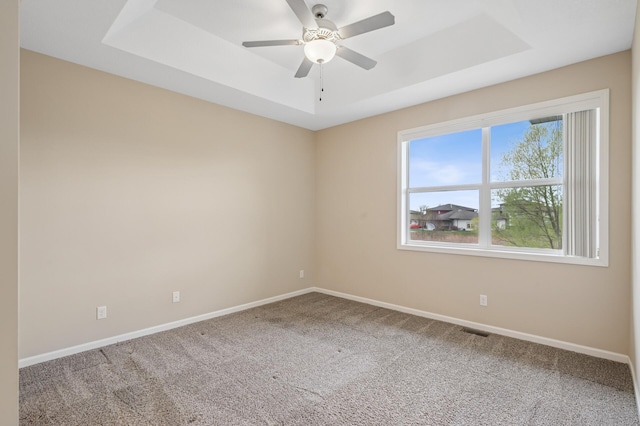 carpeted spare room featuring baseboards, a tray ceiling, visible vents, and a ceiling fan