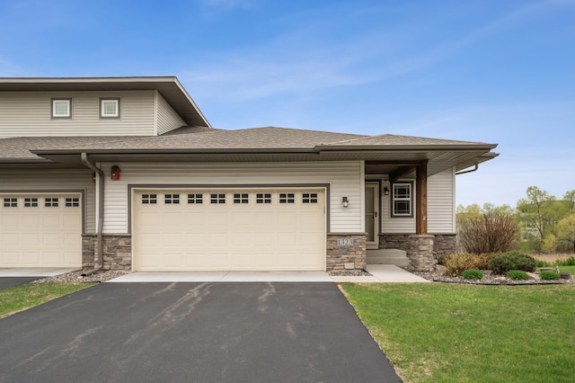 prairie-style home with aphalt driveway, a garage, stone siding, roof with shingles, and a front lawn