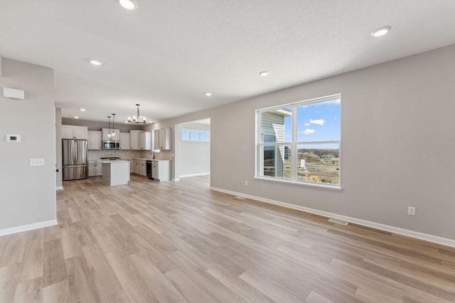 unfurnished living room featuring baseboards, a notable chandelier, visible vents, and light wood-type flooring