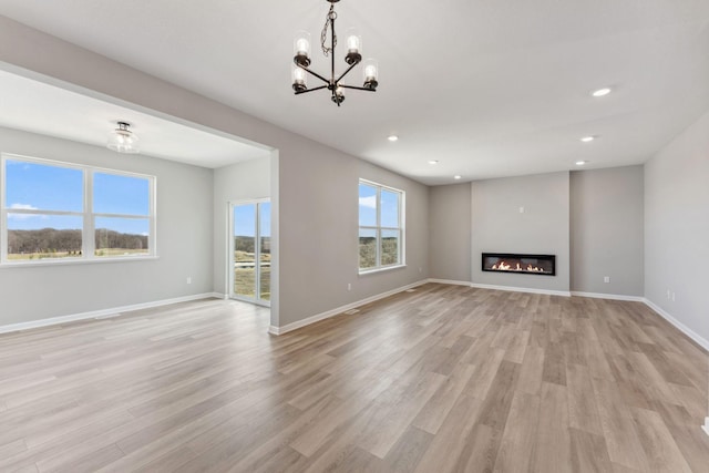 unfurnished living room featuring an inviting chandelier, light wood finished floors, a glass covered fireplace, recessed lighting, and baseboards