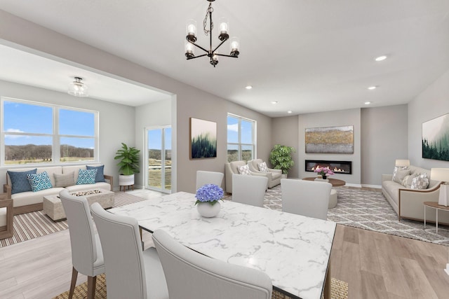 dining area featuring a notable chandelier, a glass covered fireplace, light wood-style flooring, recessed lighting, and baseboards
