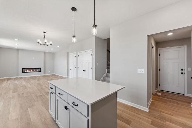 kitchen with pendant lighting, light wood-style floors, a center island, light countertops, and a notable chandelier