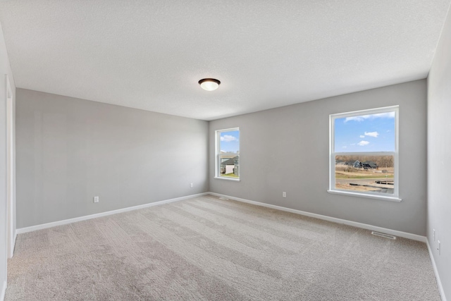empty room featuring carpet floors, baseboards, a textured ceiling, and visible vents