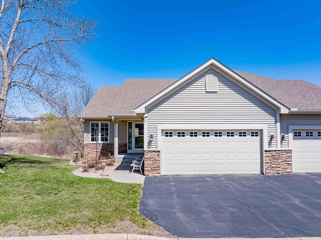view of front of property featuring an attached garage, aphalt driveway, a front lawn, and stone siding