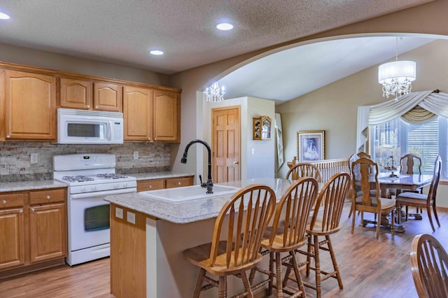 kitchen with an inviting chandelier, white appliances, light wood-type flooring, arched walkways, and backsplash