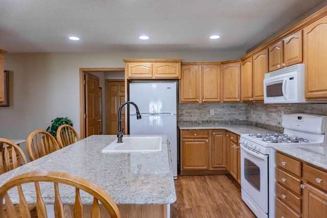 kitchen featuring backsplash, light wood-type flooring, a sink, white appliances, and an island with sink