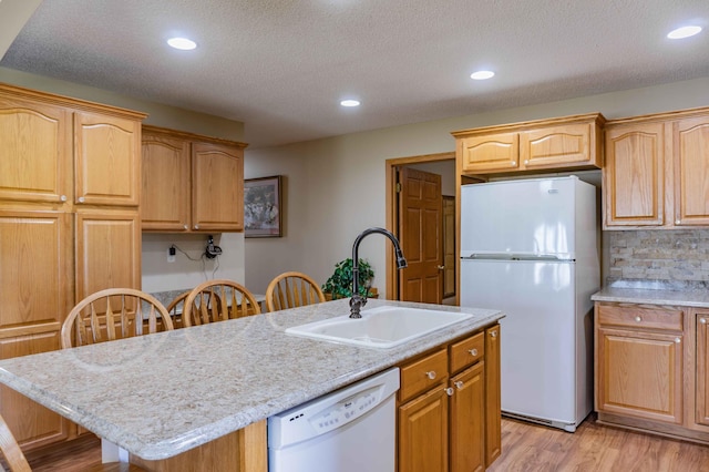 kitchen with decorative backsplash, white appliances, an island with sink, light wood-type flooring, and a sink