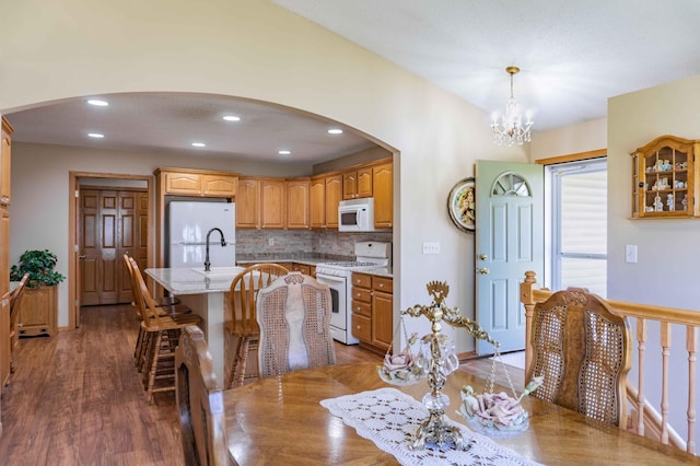 dining room with an inviting chandelier, arched walkways, recessed lighting, and wood finished floors