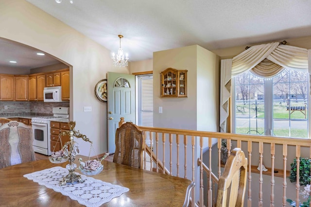 interior space featuring decorative backsplash, brown cabinetry, arched walkways, a chandelier, and white appliances