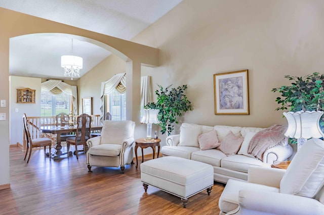 living room featuring arched walkways, a chandelier, wood finished floors, and lofted ceiling