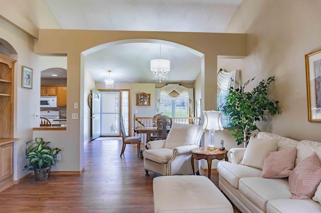 living area with an inviting chandelier, arched walkways, baseboards, vaulted ceiling, and dark wood-style floors