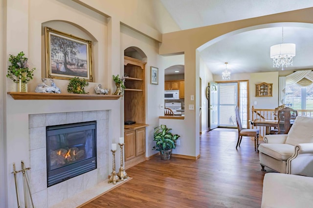 living area featuring wood finished floors, a tile fireplace, baseboards, lofted ceiling, and an inviting chandelier