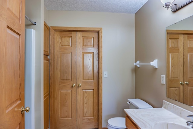 bathroom featuring toilet, a textured ceiling, a closet, and vanity