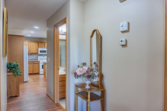 hallway with recessed lighting, a textured ceiling, and light wood finished floors