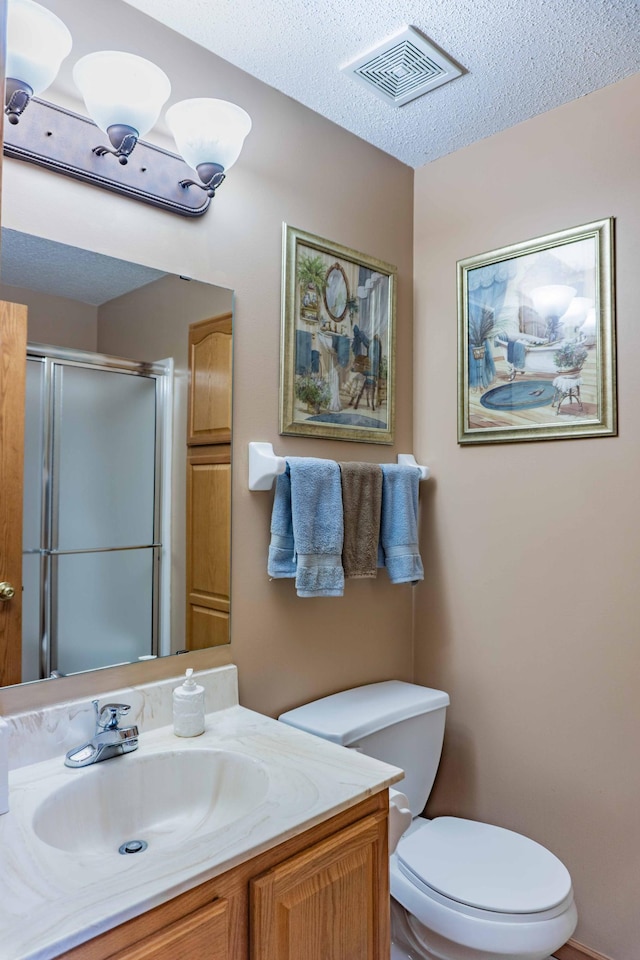 bathroom featuring vanity, toilet, a textured ceiling, a shower stall, and visible vents