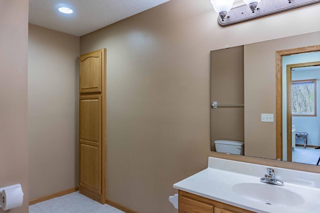 bathroom featuring toilet, a textured ceiling, baseboards, and vanity