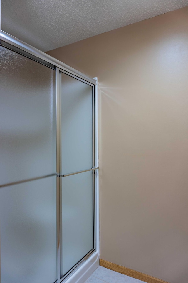 bathroom featuring an enclosed shower, a textured ceiling, and baseboards