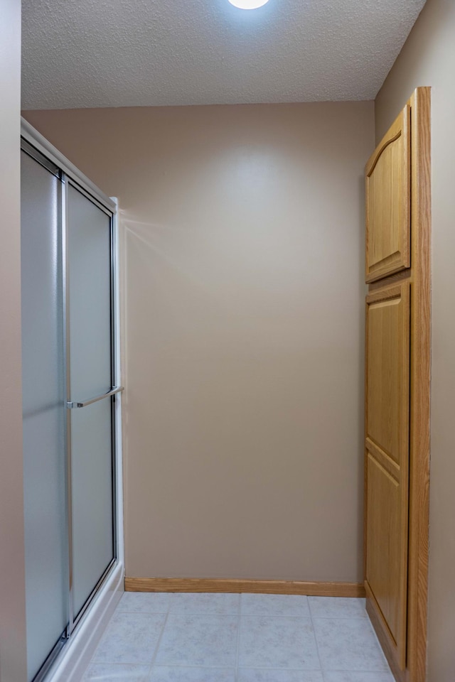 bathroom featuring an enclosed shower, a textured ceiling, and baseboards