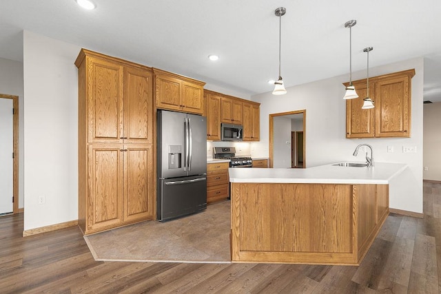 kitchen featuring brown cabinetry, a peninsula, baseboards, a sink, and stainless steel appliances