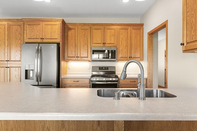 kitchen featuring a sink, appliances with stainless steel finishes, brown cabinetry, and light countertops