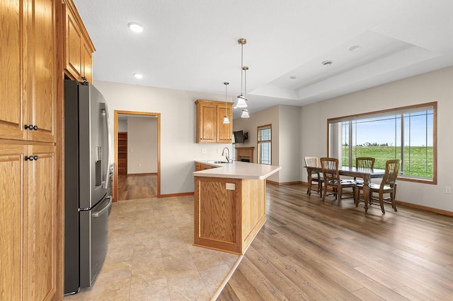 kitchen featuring a peninsula, baseboards, stainless steel fridge, and a sink