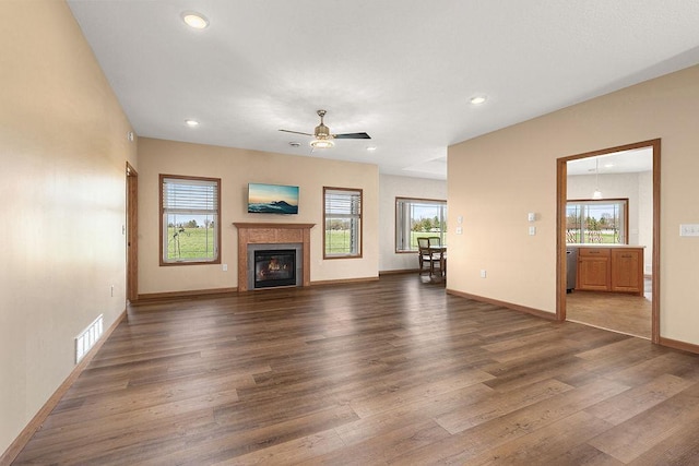 unfurnished living room featuring a glass covered fireplace, plenty of natural light, dark wood finished floors, and visible vents
