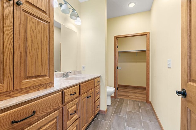 full bath with toilet, baseboards, a spacious closet, and vanity