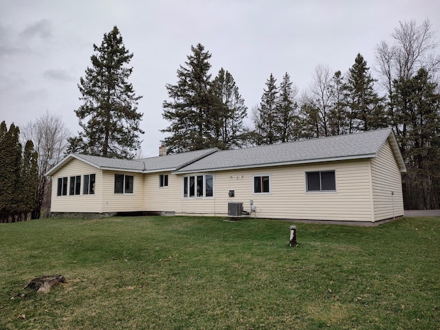 back of property with a chimney, central AC, and a lawn