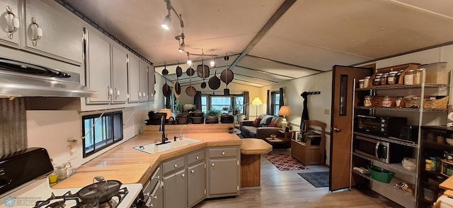 kitchen featuring lofted ceiling, a sink, a peninsula, light wood-style flooring, and open floor plan