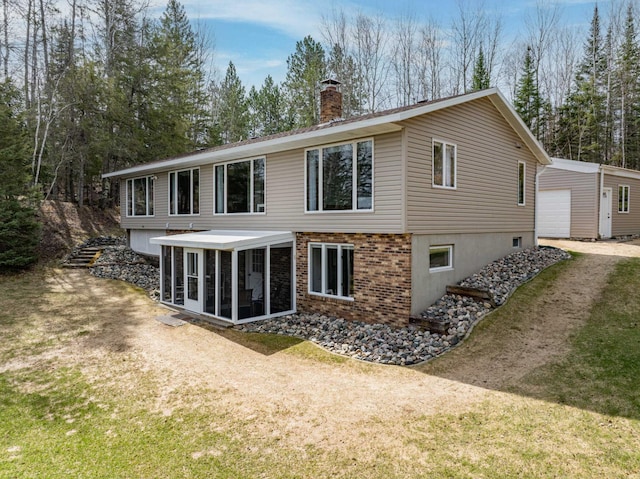 rear view of house with a chimney, a yard, an outbuilding, and a sunroom