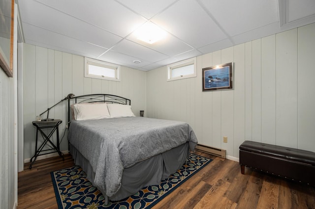 bedroom with multiple windows, a drop ceiling, dark wood-style flooring, and baseboard heating