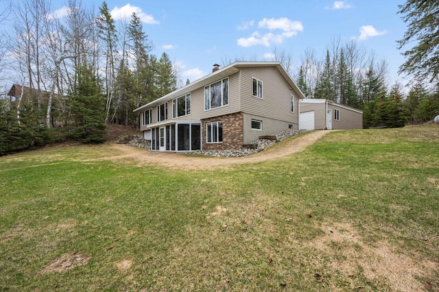 rear view of property featuring an outbuilding, a sunroom, a chimney, a yard, and a detached garage