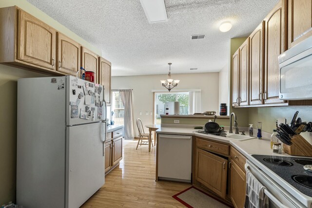 kitchen with white appliances, a sink, light wood finished floors, light countertops, and a chandelier