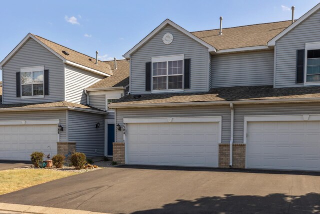 view of front of property featuring a garage, brick siding, roof with shingles, and driveway