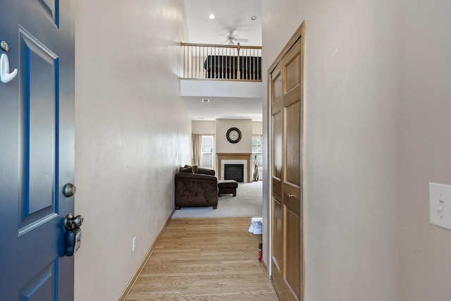 entrance foyer with ceiling fan, light wood-style floors, a glass covered fireplace, and a high ceiling