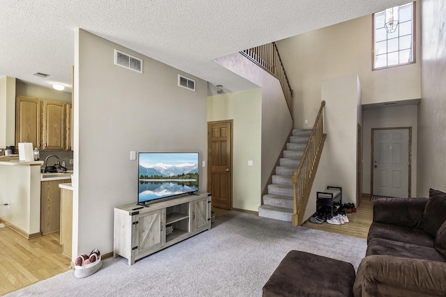 living room featuring stairway, a textured ceiling, baseboards, and light wood-style floors