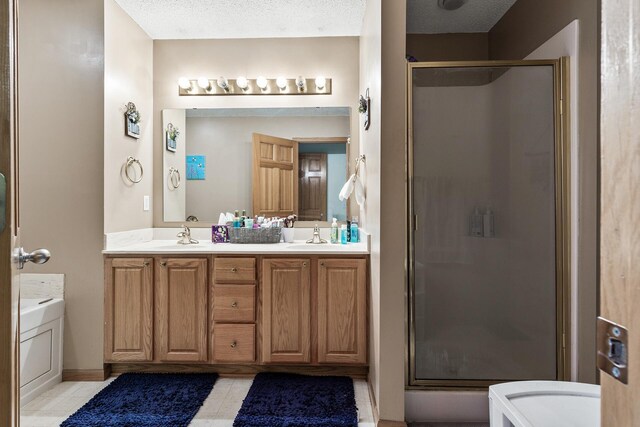 bathroom with a stall shower, double vanity, a textured ceiling, and tile patterned floors