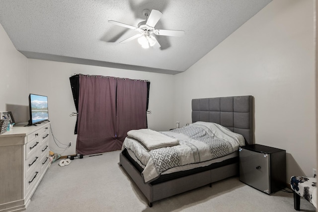 bedroom with light colored carpet, lofted ceiling, freestanding refrigerator, a textured ceiling, and ceiling fan