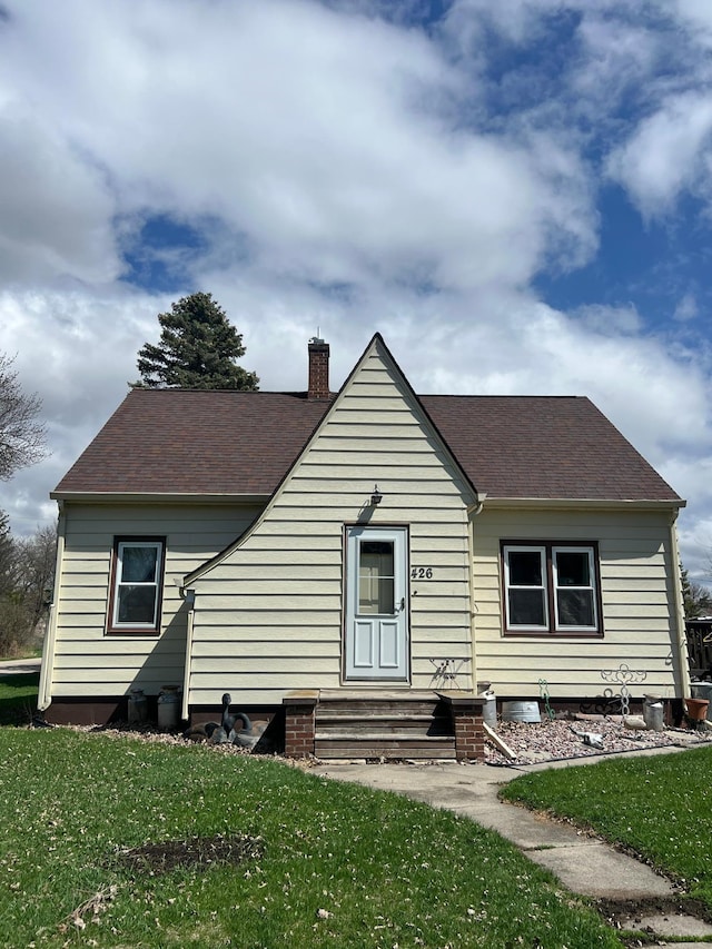 exterior space with a yard, a shingled roof, entry steps, and a chimney