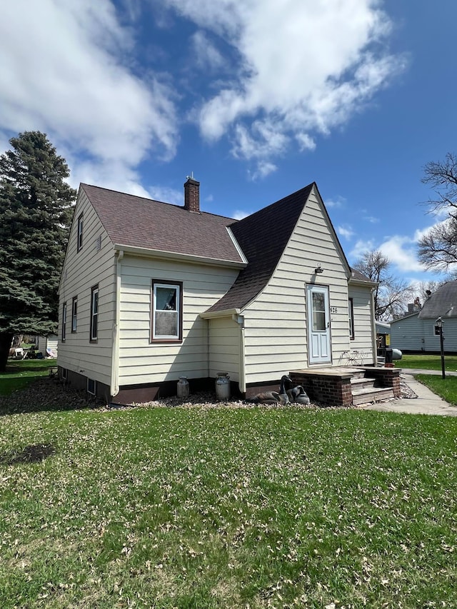rear view of house with a chimney, a yard, and roof with shingles