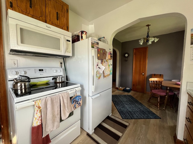 kitchen featuring arched walkways, white appliances, a chandelier, brown cabinetry, and light wood-type flooring