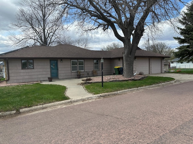 ranch-style house featuring driveway, roof with shingles, a front yard, and an attached garage