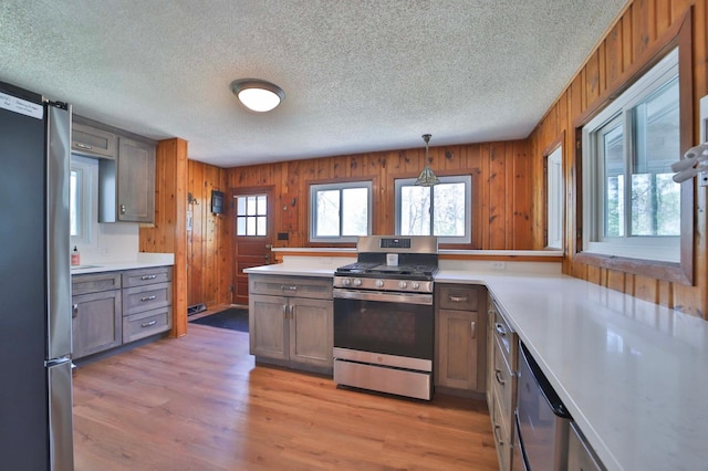 kitchen with stainless steel appliances, a textured ceiling, light countertops, light wood-style flooring, and wooden walls